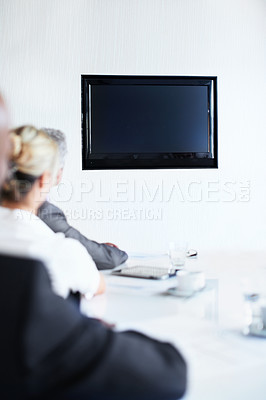 Buy stock photo Over the shoulder shot of a group of businesspeople sitting around a boardroom table looking at a blank monitor