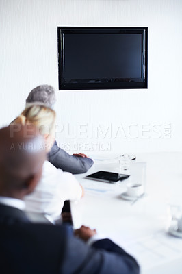 Buy stock photo Over the shoulder shot of a diverse group of businesspeople sitting around a boardroom table looking at a blank monitor