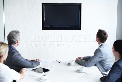 Buy stock photo Over the shoulder shot of a group of businesspeople sitting around a boardroom table looking at a blank monitor