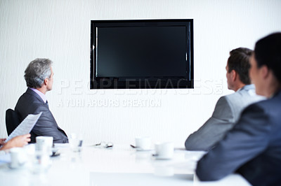 Buy stock photo Rearview shot of a group of businesspeople sitting around a boardroom table looking at a blank monitor