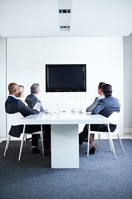 Buy stock photo Full length shot of a group of businesspeople sitting around a boardroom table looking at a blank monitor