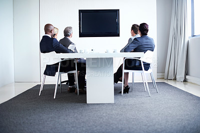 Buy stock photo Full length shot of a group of businesspeople sitting around a boardroom table looking at a blank monitor