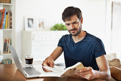 Buy stock photo A handsome young man working on his laptop while reading a book
