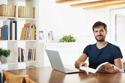 Buy stock photo Portrait of a handsome young man working on his laptop while reading a book
