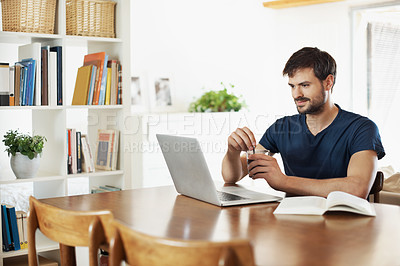 Buy stock photo A handsome young man working on his laptop while reading a book