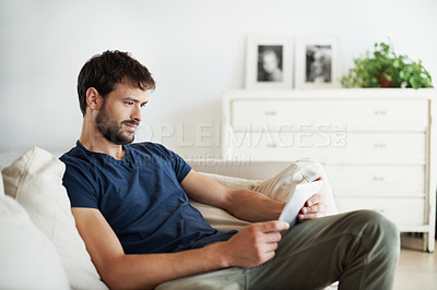 Buy stock photo A handsome young man using his tablet while sitting at home