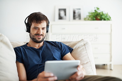 Buy stock photo A handsome young man listening to music on his tablet while sitting at home