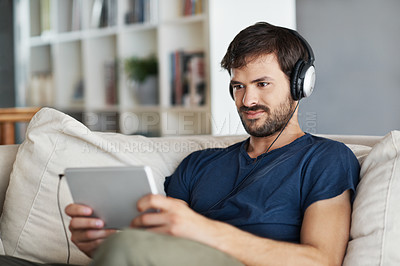 Buy stock photo A handsome young man listening to music on his tablet while sitting at home