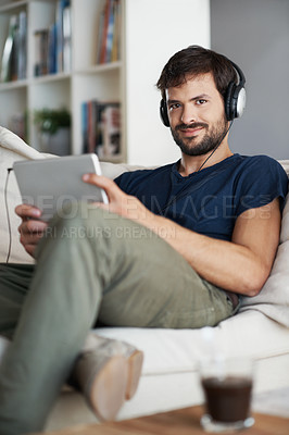 Buy stock photo Portrait of a handsome young man listening to music on his tablet while sitting at home