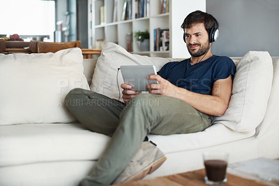 Buy stock photo A handsome young man listening to music on his tablet while sitting at home