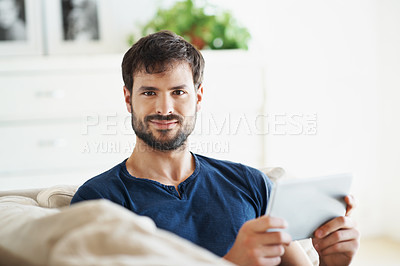Buy stock photo Portrait of a handsome young man using his tablet while sitting on the sofa