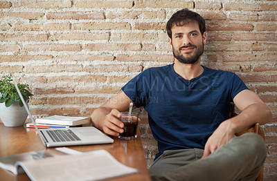 Buy stock photo Portrait of a handsome young man working on his laptop while reading a magazine