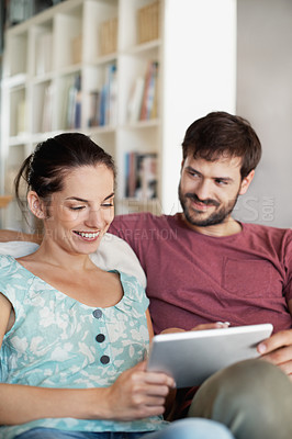 Buy stock photo A young couple sharing their tablet while relaxing on the sofa