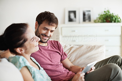 Buy stock photo A young couple sharing their tablet while relaxing on the sofa