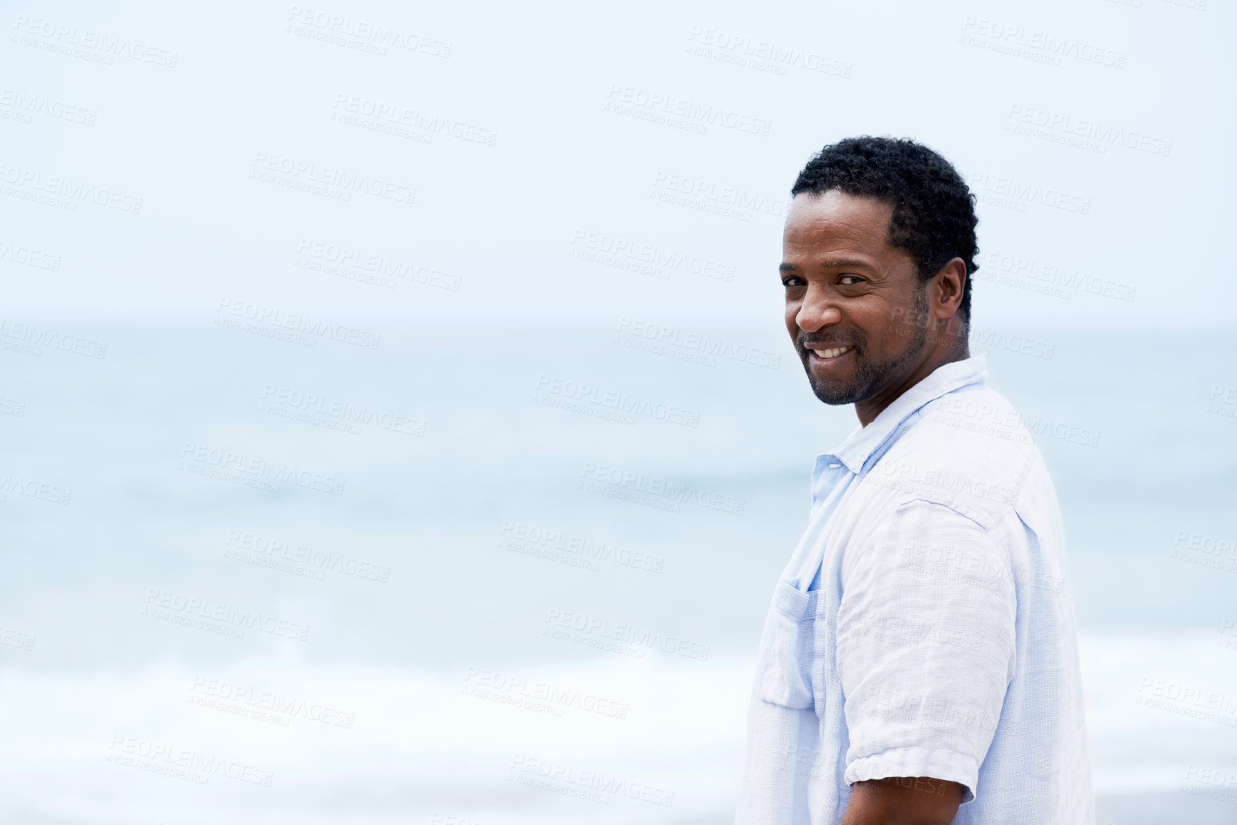 Buy stock photo A handsome young African-American man standing on the beach looking at the camera