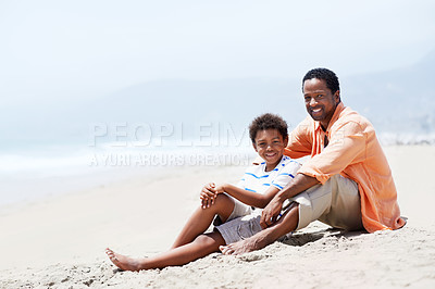 Buy stock photo An African-American father and son sitting by the sea on an overcast day