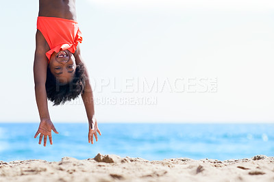 Buy stock photo A little African-American girl in an orange swimsuit hanging upside down on the beach