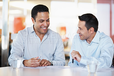 Buy stock photo Two smiling businessmen discussing some paperwork together at a desk