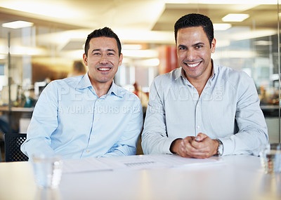 Buy stock photo A portrait of two business partners sitting at a desk in the office and smiling