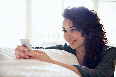 Buy stock photo A pretty young woman sending a text message in her bedroom