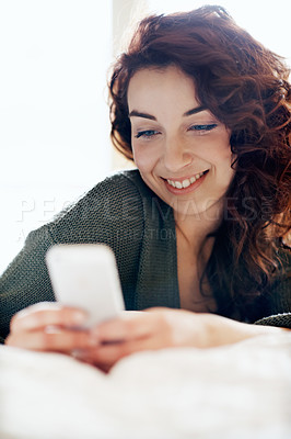 Buy stock photo A pretty young woman sending a text message in her bedroom