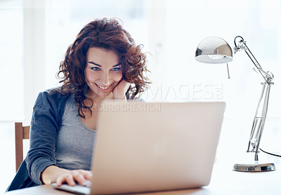 Buy stock photo A pretty young woman browsing the internet on her laptop at home