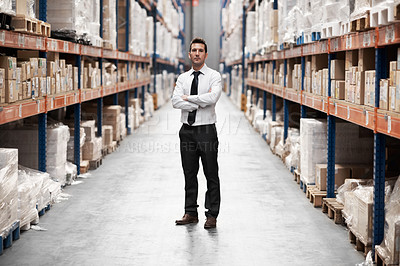 Buy stock photo Handsome warehouse manager standing in a warehouse surrounded by boxes with his arms folded