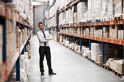 Buy stock photo Handsome warehouse manager standing in a warehouse surrounded by boxes with his arms folded
