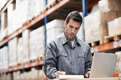 Buy stock photo A young man using his laptop and taking notes while working in a storehouse
