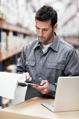 Buy stock photo A young man using his notebook and taking notes while working in a storehouse