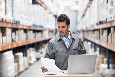 Buy stock photo A young man using his notebook and looking over his notes while working in a warehouse