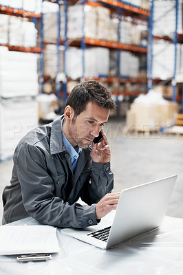 Buy stock photo A young man in a warehouse taking orders on his cellphone and recording them on his notebook