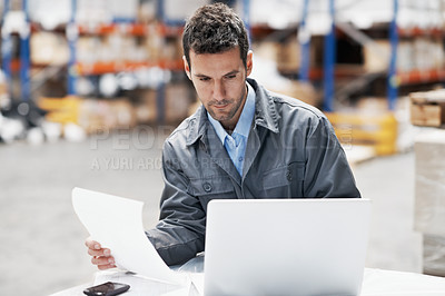 Buy stock photo A young man using his notebook and looking over his notes while working in a storehouse