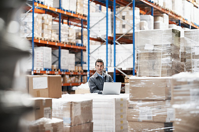 Buy stock photo Portrait of a young man working on his laptop while sitting in a storehouse