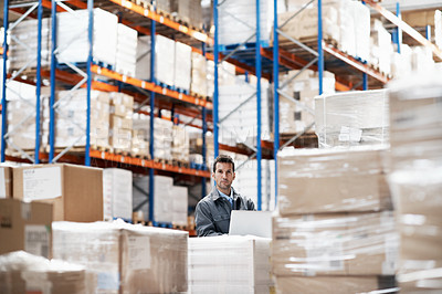 Buy stock photo Portrait of a handsome young man working on his notebook while sitting in a storehouse