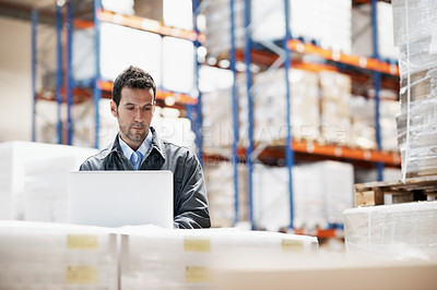 Buy stock photo A young man working on his laptop in a warehouse