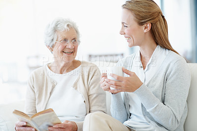 Buy stock photo Reading book, coffee and senior mother with woman laughing, bonding together and connection in home. Novel, elderly parent and adult daughter with drink in living room, funny story and happy family