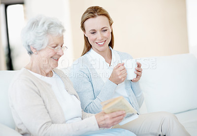 Buy stock photo Reading book, coffee and senior mother with women bonding, relax together and connection in home. Novel, elderly parent and adult daughter with drink in lounge, story recommendation and happy family