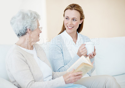 Buy stock photo Reading book, coffee and senior mother with women for love, bonding together and connection in home. Novel, elderly parent and adult daughter with drink in living room, share story and happy family