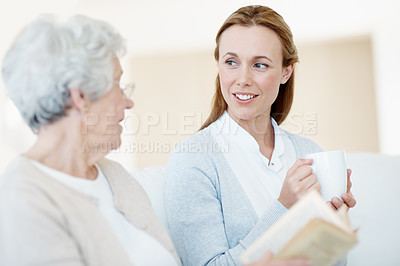 Buy stock photo Reading book, tea and senior mother with women for care, bonding together and conversation in home. Novel, elderly parent and adult daughter with drink in living room, gossip story and happy family