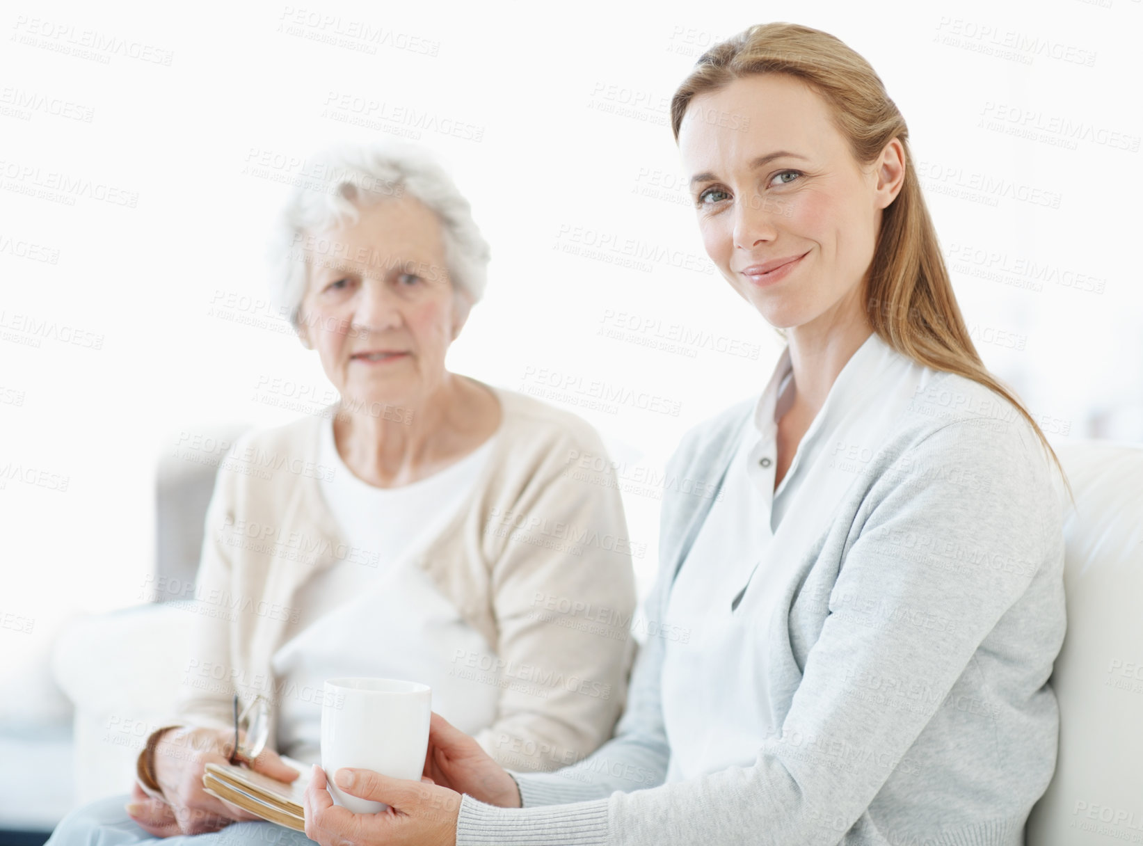 Buy stock photo Love, senior mother and adult daughter with coffee in home, smile and connection together on weekend. Elderly parent, happy women and bonding in living room with drink, book and family portrait