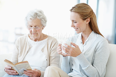 Buy stock photo Reading book, coffee and senior mother with woman for relax, bonding together and connection in home. Novel, elderly parent and adult daughter with drink in living room, story and happy family