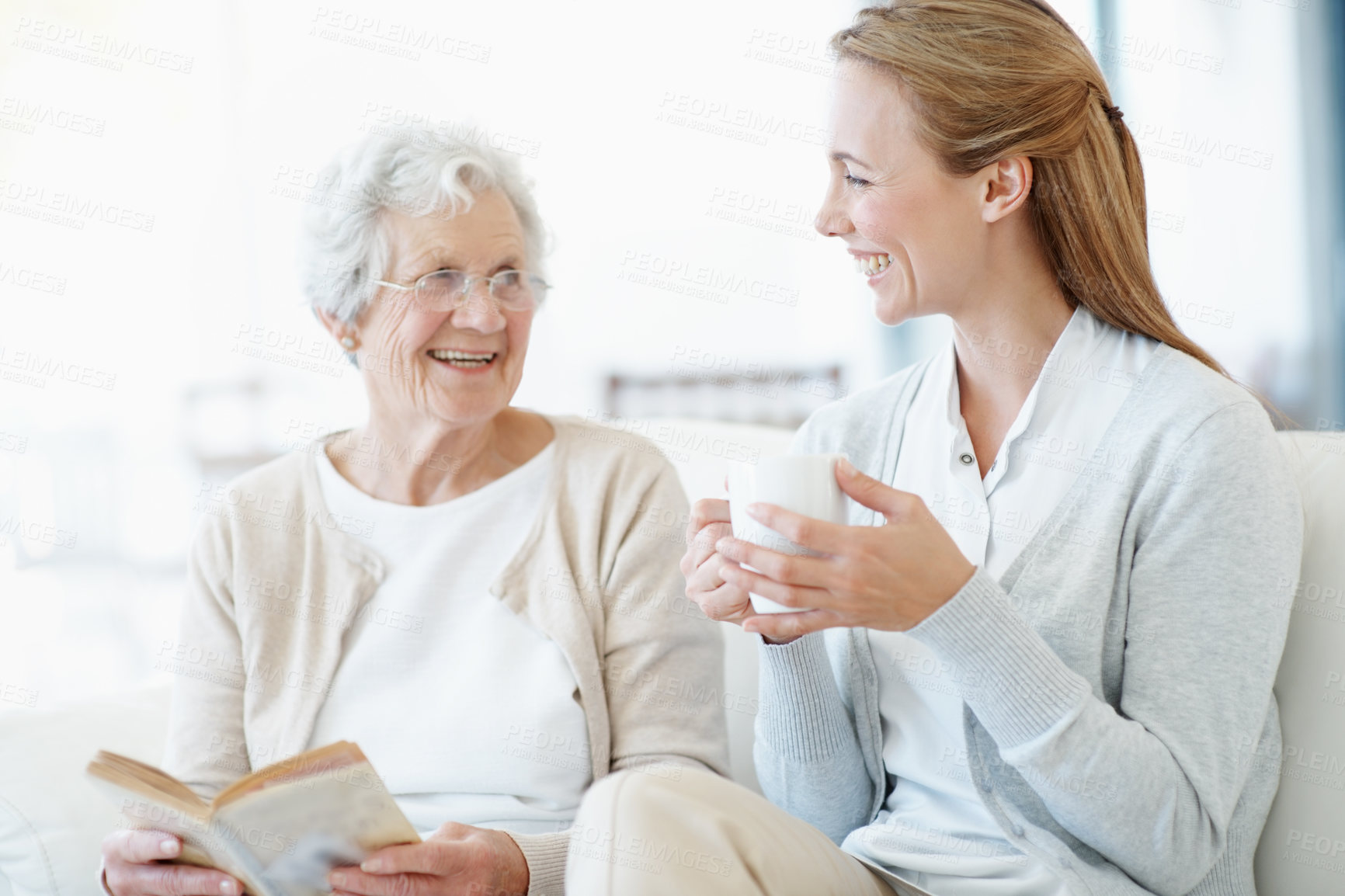 Buy stock photo Reading book, tea and senior mother with women laughing, bonding together and connection in home. Novel, elderly parent and adult daughter with drink in living room, funny story and happy family