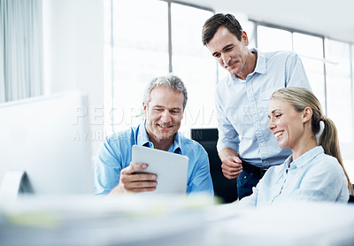 Buy stock photo Three businesspeople looking at a digital tablet while working together in their office