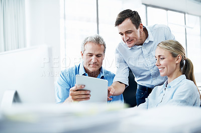 Buy stock photo Three businesspeople looking at a digital tablet while working together in their office