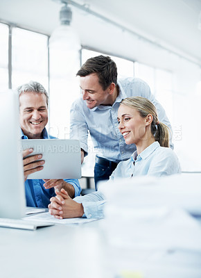 Buy stock photo Three businesspeople looking at a digital tablet while working together in their office