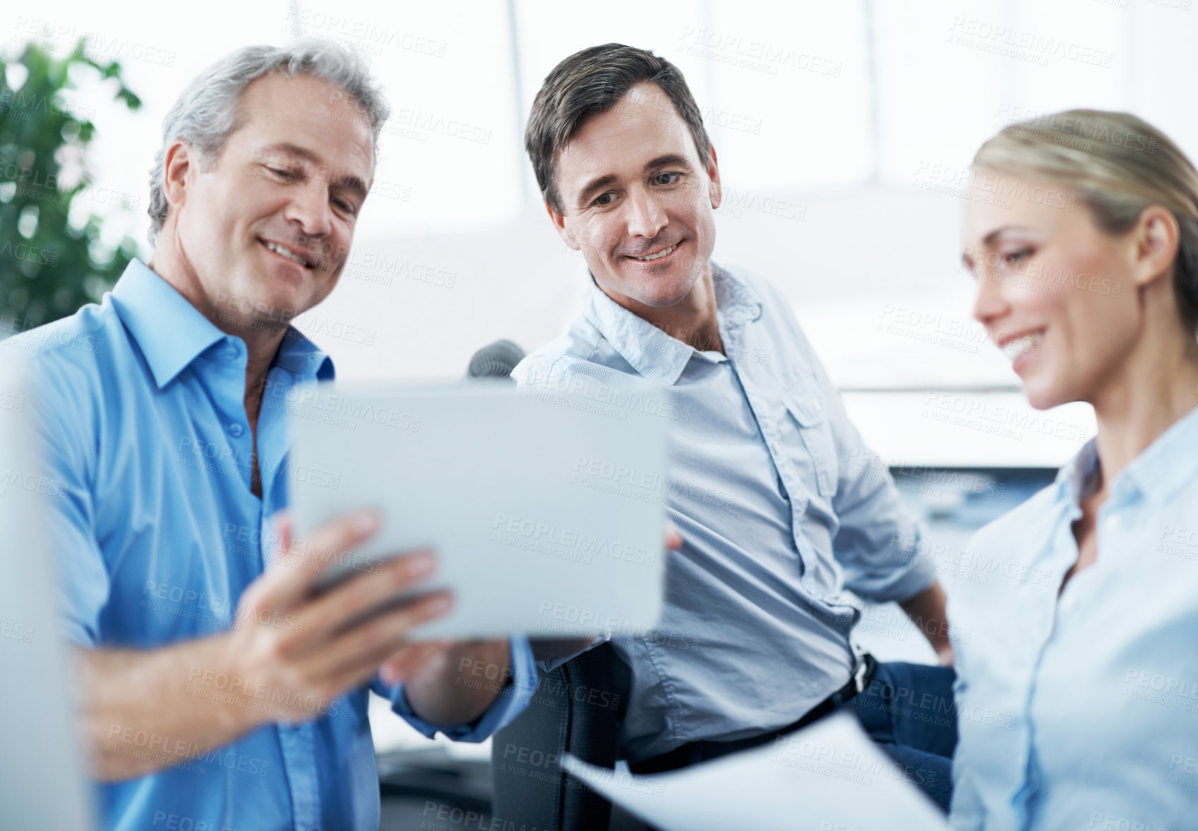 Buy stock photo Three businesspeople looking at a digital tablet while working together in their office