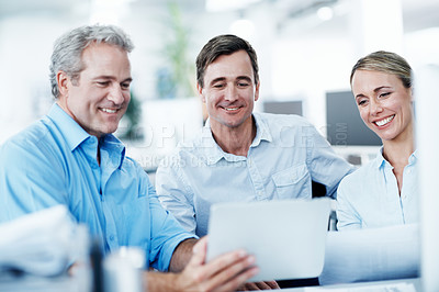 Buy stock photo Three businesspeople looking at a digital tablet while working together in their office