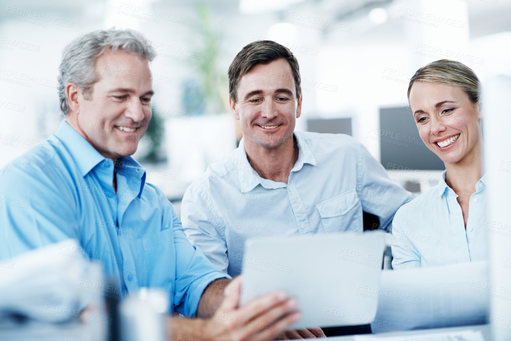 Buy stock photo Three businesspeople looking at a digital tablet while working together in their office