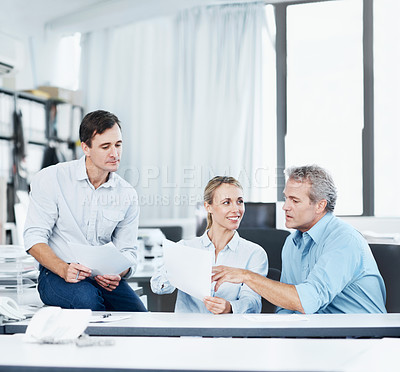 Buy stock photo Three coworkers talking while looking over some documents in the office